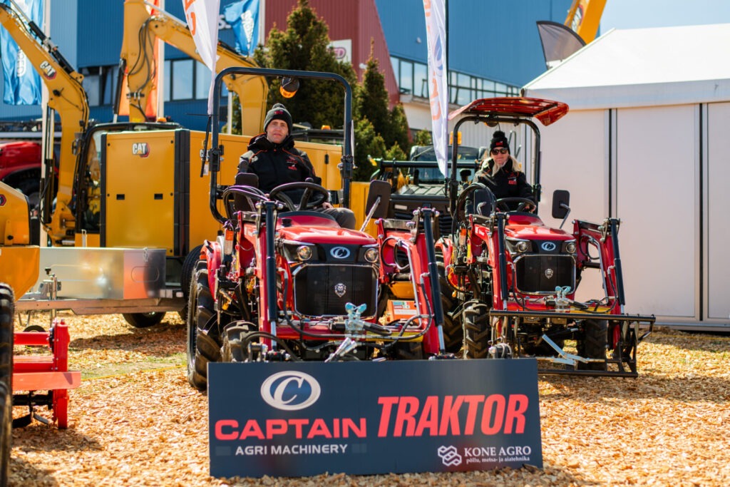 Kaks inimest istuvad punastel traktoritel väljanäitusel sildi ees, millel seisab "Kapten Traktor Agri Machinery Kone Agro", tõenäoliselt Maamessil 2026. Taustal on näha ehitus- ja põllumajandusseadmeid.